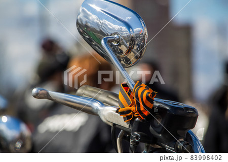 The mirror of the motorcycle is decorated for Victory Day. Black-orange ribbon as a symbol of Victory Day. The mirror of the motorcycle is decorated for Victory Day. Black-orange ribbon as a symbol of Victory Day. 83998402