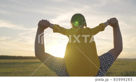 cheerful little kid rides his father at sunset, joyful child sits on his dad shoulders in sunshine of sun, happy family, girl with parent on a weekend trip, childhood dream of being pilot and flying cheerful little kid rides his father at sunset, joyful child sits on his dad shoulders in sunshine of sun, happy family, girl with parent on a weekend trip, childhood dream of being pilot and flying 83999265