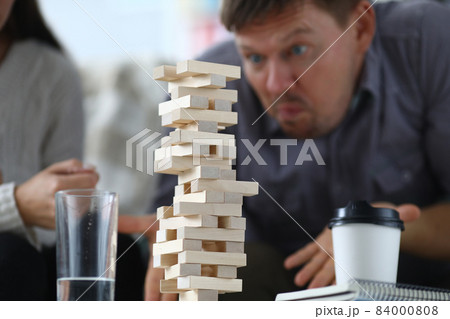 Man assembles a tall tower from wooden rectangular blocks 84000808
