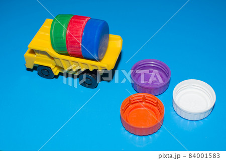 Toy dump truck unloads colorful plastic caps on blue background. Toy dump truck unloads colorful plastic caps on blue background. 84001583