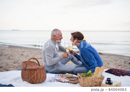 Happy senior couple in love sitting on blanket and having picnic outdoors on beach by sea. 84004063