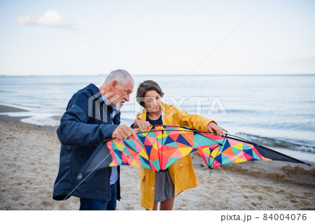 Senior man and his preteen granddaughter preparing kite for flying on sandy beach. Senior man and his preteen granddaughter preparing kite for flying on sandy beach. 84004076