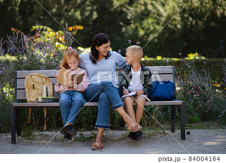 Happy senior woman with grandchildren sitting on bench and helping with homework outdoors in park. Happy senior woman with grandchildren sitting on bench and helping with homework outdoors in park. 84004164