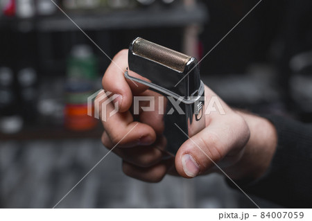 The hand of a barber or hairdresser holds an automatic clipper for cutting and shaving close-up against the background of the salon 84007059
