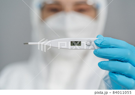 doctor in PPE suit holding digital thermometer with normal temperature 84011055