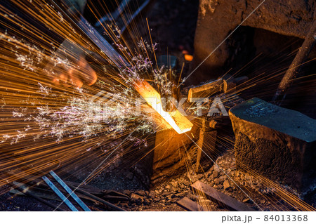 Blacksmith forging the molten metal on the anvil with spark fireworks 84013368