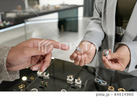 Young woman holding two rings while male client pointing at one of them Young woman holding two rings while male client pointing at one of them 84014960