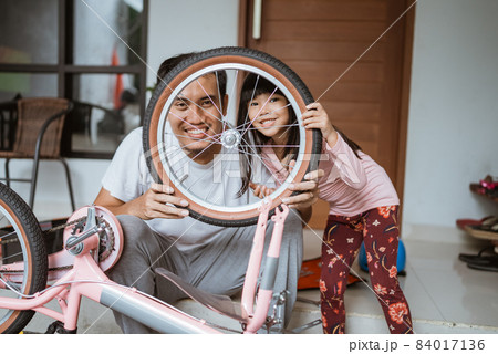 Smiling father and daughter looking at camera between bicycle wheels Smiling father and daughter looking at camera between bicycle wheels 84017136