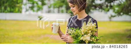 Young woman holds in her hands with a paper tumbler with coffee or tea BANNER, LONG FORMAT 84018265
