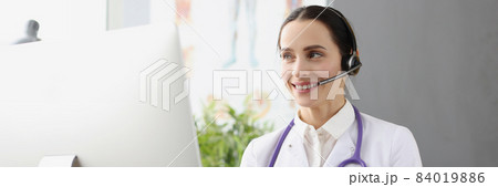 Doctor in headphones with microphone holding x ray in front of computer screen 84019886