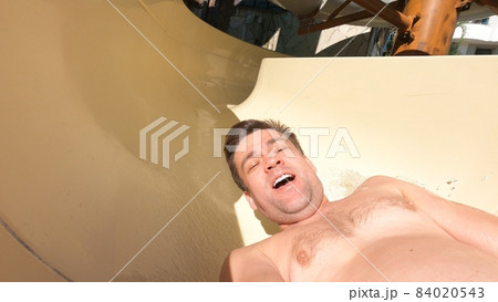a man in a camera in his hands rolls down a slide in a water park.  84020543