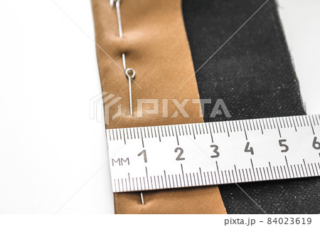 Processing of the seam with an oblique brown silk label. Close-up, wrong side. The seam is pinned with pins, the process of measuring the width of the seam. Concept: atelier, sewing hobby. Processing of the seam with an oblique brown silk label. Close-up, wrong side. The seam is pinned with pins, the process of measuring the width of the seam. Concept: atelier, sewing hobby. 84023619