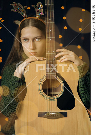 Beautiful teenage girl in Christmas antlers and a green sweater with guitar 84026546