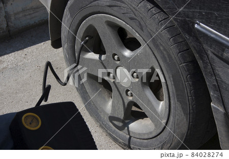 The driver pumps up the wheel of a black car with the help of a compressor The driver pumps up the wheel of a black car with the help of a compressor 84028274