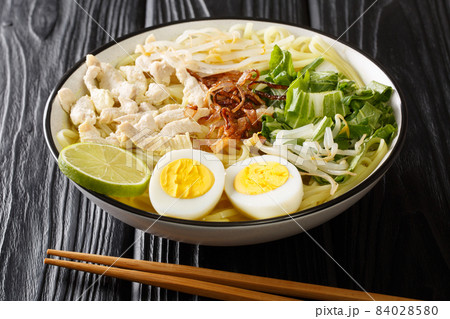 Indonesian 'Soto Ayam' Chicken Noodle Soup in a spicy broth close up in the plate. Horizontal Indonesian 'Soto Ayam' Chicken Noodle Soup in a spicy broth close up in the plate. Horizontal 84028580