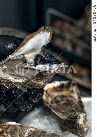 Raw open oyster in hand with black gloves Raw open oyster in hand with black gloves 84028726