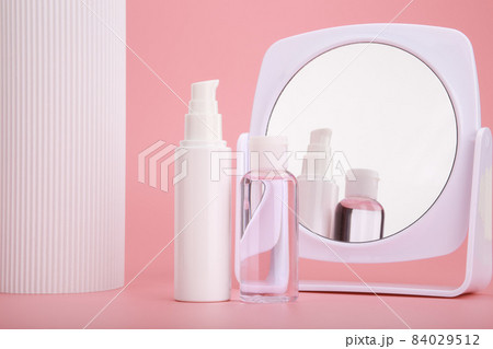 Set of two cosmetic bottles next to white column and mirror against bright pink background  84029512