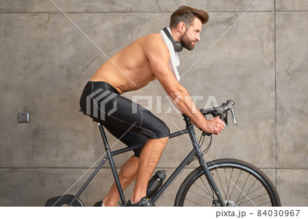 Athletic young man riding stationery bike against the wall 84030967