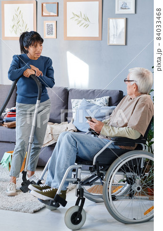 Senior man using wheelchair talking to housemaid who cleaning the room, he giving her instructions before work Senior man using wheelchair talking to housemaid who cleaning the room, he giving her instructions before work 84033468