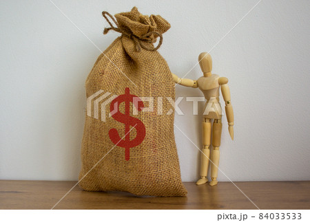 Wooden model of a man near large canvas bag with a dollar sign. 84033533
