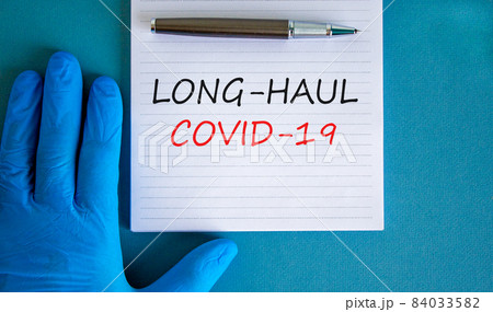COVID-19 long-haul covid symptoms symbol. White card with words Long-haul covid-19. Doctor hand, pen, blue background, copy space. Medical, COVID-19 long-haul covid-19 symptoms concept. 84033582