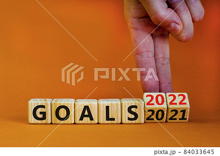 Planning 2022 goals new year symbol. Businessman turns wooden cubes and changes words 'Goals 2021' to 'Goals 2022'. Beautiful orange background, copy space. Business, 2022 goals new year concept. Planning 2022 goals new year symbol. Businessman turns wooden cubes and changes words 'Goals 2021' to 'Goals 2022'. Beautiful orange background, copy space. Business, 2022 goals new year concept. 84033645