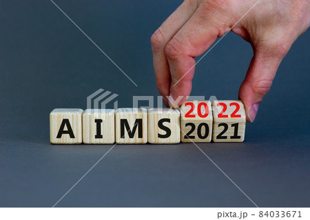 Business concept of planning 2022 aims new year. Businessman turns a wooden cube and changes words 'Aims 2021' to 'Aims 2022'. Beautiful grey background, copy space. Business, 2022 aims concept. Business concept of planning 2022 aims new year. Businessman turns a wooden cube and changes words 'Aims 2021' to 'Aims 2022'. Beautiful grey background, copy space. Business, 2022 aims concept. 84033671