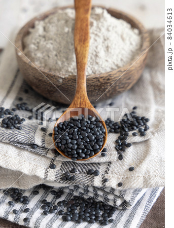Bowl with a spoon of black lentils flour and beans on white wooden table close up 84034613