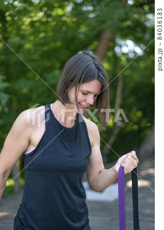 Fitness woman doing exercise for biceps with resistance band outdoors. Athletic girl workout. Close up Fitness woman doing exercise for biceps with resistance band outdoors. Athletic girl workout. Close up 84036183