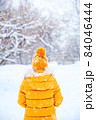 Back view of young woman wearing yellow jacket walks in snowy park 84046444