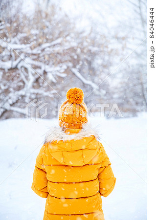Back view of young woman wearing yellow jacket walks in snowy park 84046444