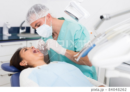 Dentist man examining a latin female patient teeth Dentist man examining a latin female patient teeth 84048262