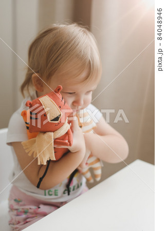 Little baby girl playing with funny small tiger toy, symbol of new 2022 in a sunny nursery 84048946
