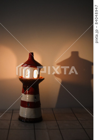 burning candle in a candlestick in the shape of a lighthouse with a shadow, cozy warm atmosphere 84048947