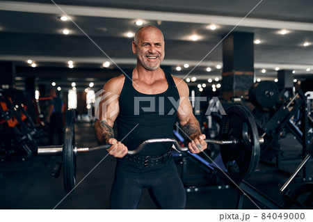 Muscular bald man working out in gym doing exercises with barbell at biceps. Bodybuilding concept 84049000
