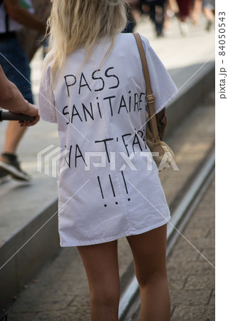 portrait on back view of woman protesting in the street with text on shirt in french, pass sanitaire vat faire !!!, in English, sanitary pass F... you !!!  84050543