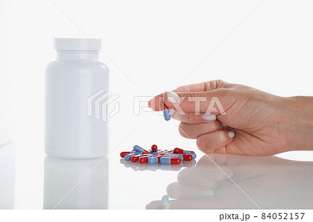 Womans hand hold one jelly capsule bunch of pill scattered on surface Womans hand hold one jelly capsule bunch of pill scattered on surface 84052157