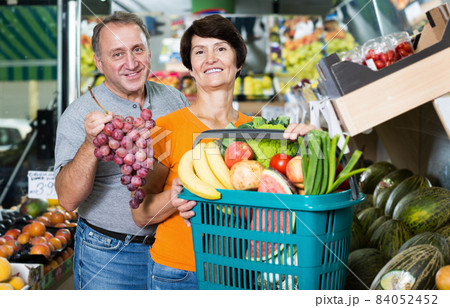 Happy mature couple standing with basket in food store Happy mature couple standing with basket in food store 84052452