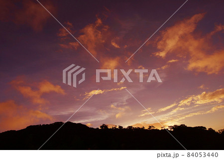 伊豆のダイナミックな夕焼けの空。周りを赤く染めながら山肌の木々をシルエットにし露にして 84053440