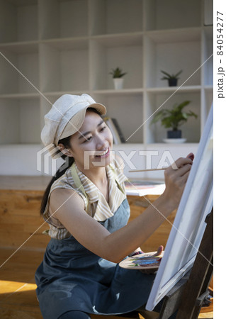 Asian woman painter sitting in front of the canvas and painting with water color at workshop. Asian woman painter sitting in front of the canvas and painting with water color at workshop. 84054277