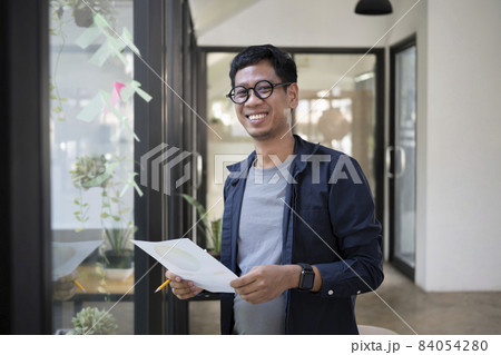 Young creative man standing in modern office and smiling to camera. Young creative man standing in modern office and smiling to camera. 84054280