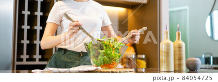 salad concept the woman with white t-shirt and dark green pants standing at the kitchen and making a bowl of green salad salad concept the woman with white t-shirt and dark green pants standing at the kitchen and making a bowl of green salad 84054725