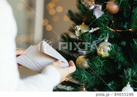Hand holding stack of craft paper envelopes for christmas greeting card invitation design on christmas tree background with bokeh. Hand holding stack of craft paper envelopes for christmas greeting card invitation design on christmas tree background with bokeh. 84055296