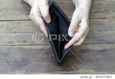 A woman shows an empty wallet in which there is no money on an old wooden table. Concept of economic crisis, poverty, ruin, unemployment 84055863