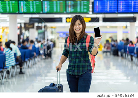 Asian traveler with luggage showing the smart mobile phone for check-in over the flight board at the flight information screen in modern an airport, travel and transportation with technology concept. 84056334