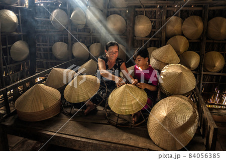 Vietnamese Old woman craftsman teaching the grandchild making the traditional vietnam hat in the old traditional house in Ap Thoi Phuoc village, Hochiminh city, Vietnam, traditional artist concept Vietnamese Old woman craftsman teaching the grandchild making the traditional vietnam hat in the old traditional house in Ap Thoi Phuoc village, Hochiminh city, Vietnam, traditional artist concept 84056385