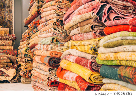 Stack of traditional oriental carpets and rugs as background with copy space. Multicolored ornamental carpets at carpet store. Popular touristic souvenir. Selective focus Stack of traditional oriental carpets and rugs as background with copy space. Multicolored ornamental carpets at carpet store. Popular touristic souvenir. Selective focus 84056865