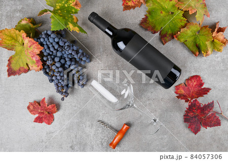 Red wine bottle with black label mockup with bunch of grape, green and red fall grape's leaves on gray background Red wine bottle with black label mockup with bunch of grape, green and red fall grape's leaves on gray background 84057306