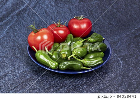 Red tomatoes and green peppers on a blue plate on a piece of slate. Vegan food concept 84058441