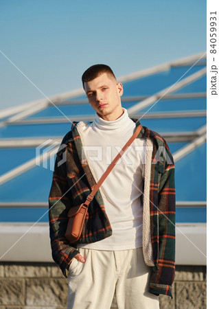 Young man in plaid jacket, white turtleneck and trousers with hand in the pocket on the street 84059931